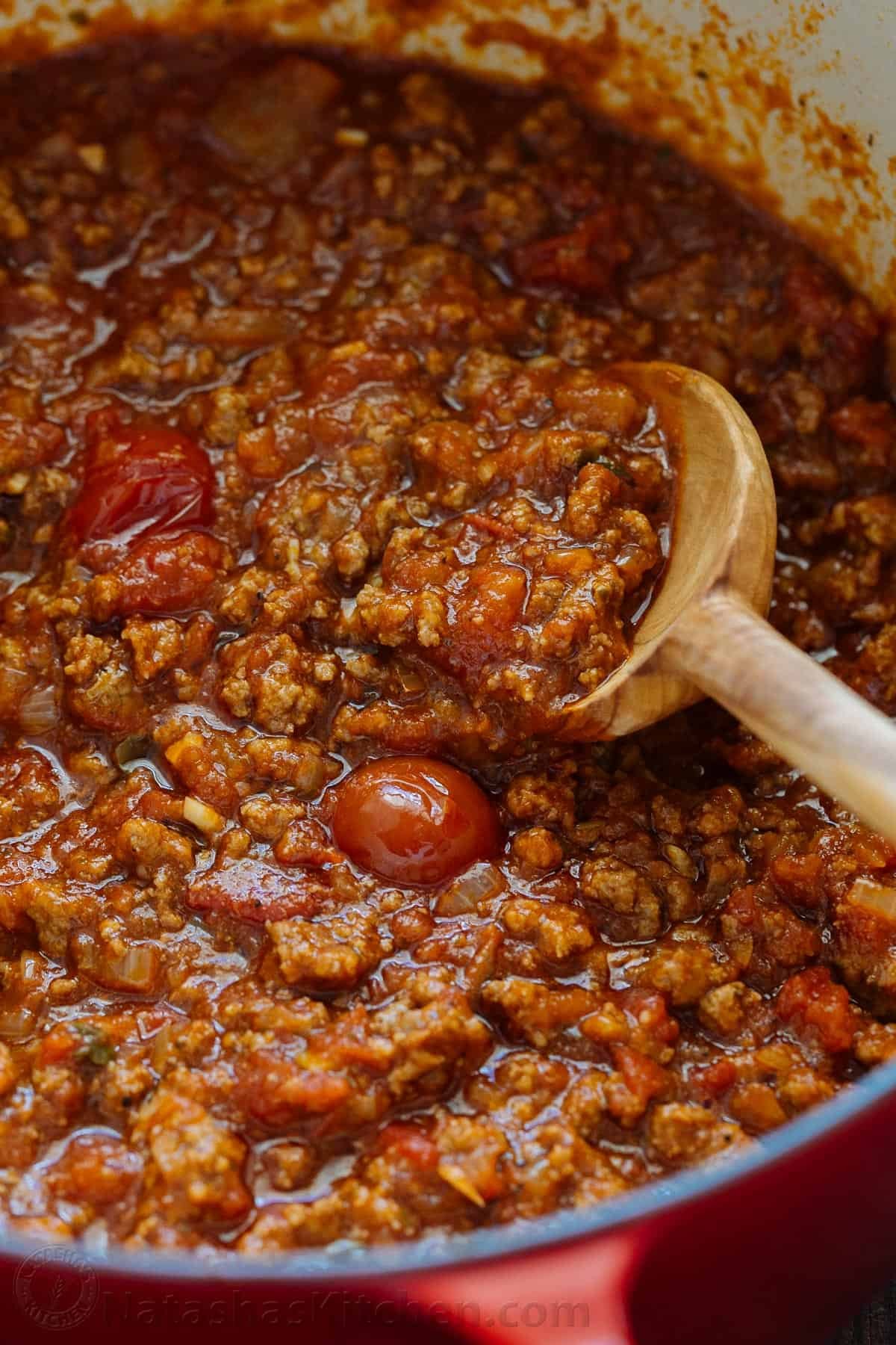 A close up of meat sauce for spaghetti with a wooden spoon in the pot. 