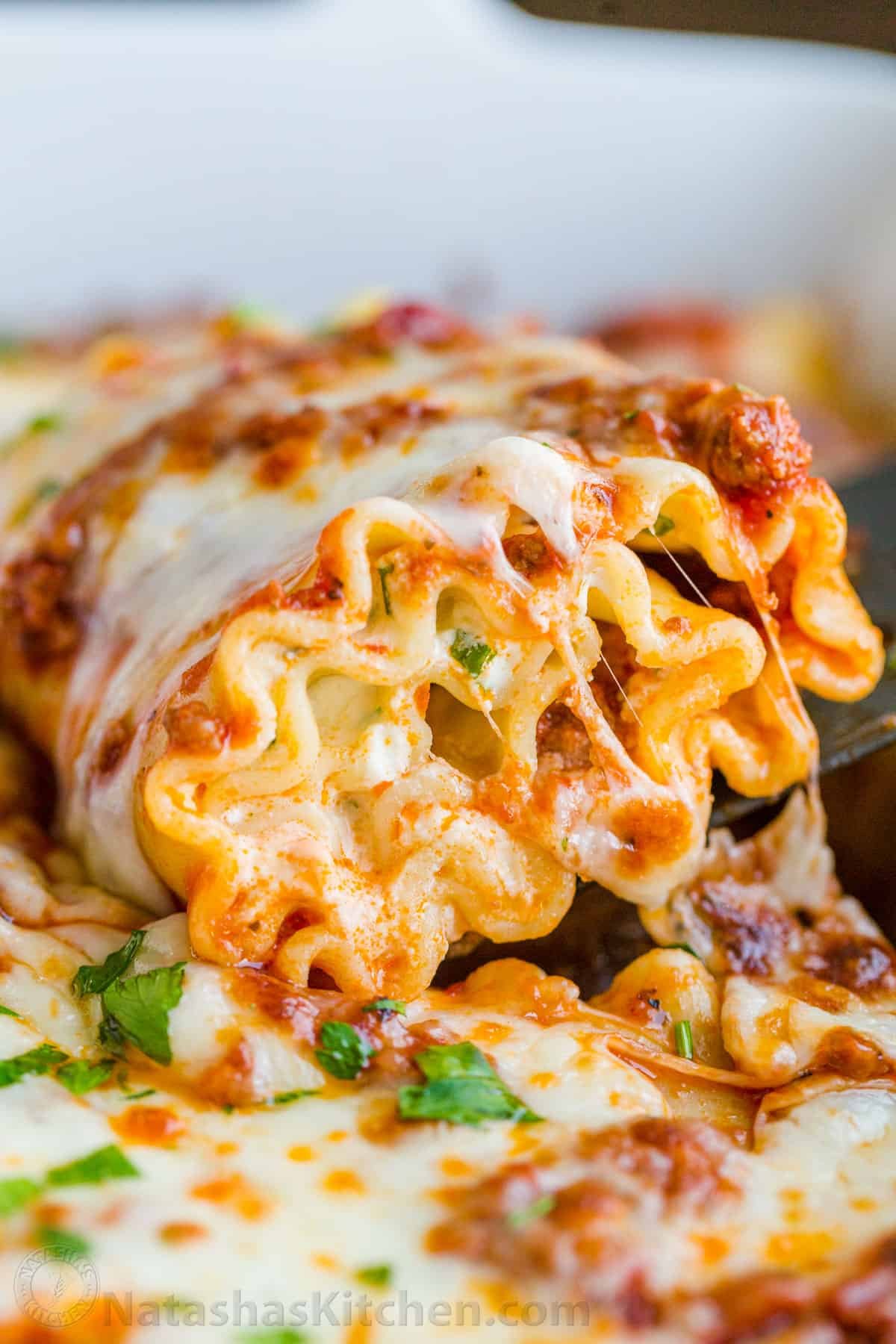 Lasagna roll being scooped out of casserole dish with cheese pull