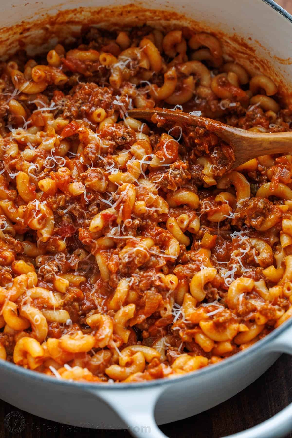 Recipe or American Goulash stirred in a white dutch oven with wooden spoon