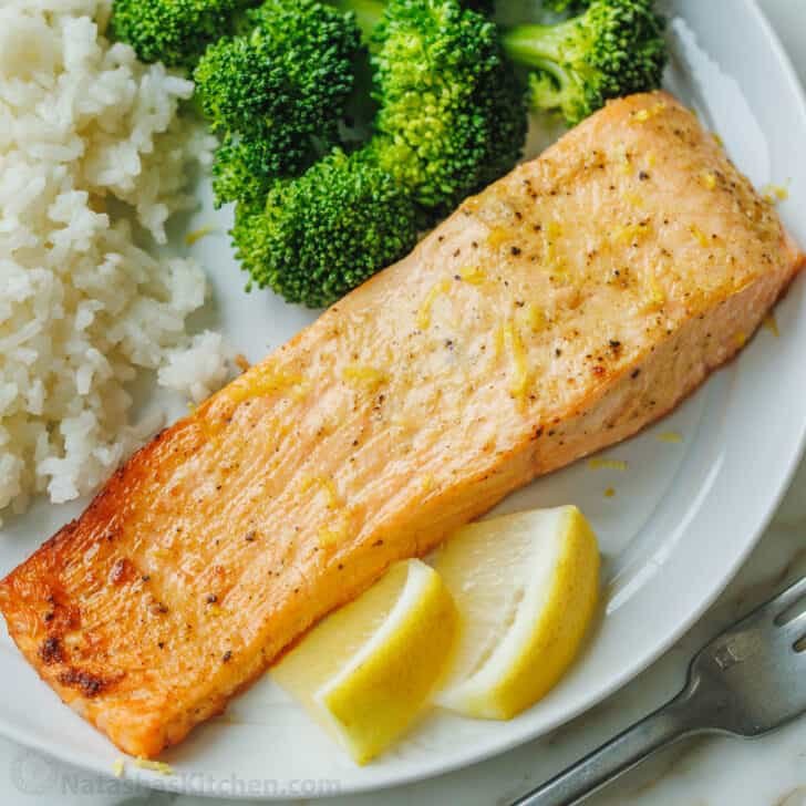 Air fryer salmon fillet on a white plate served with a side of rice and broccoli, with lemon wedges for garnish.