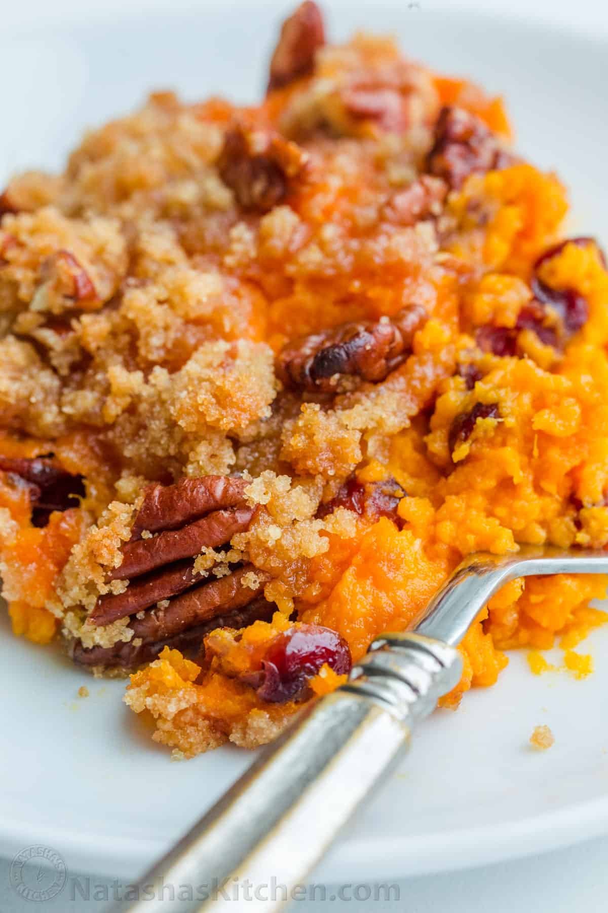 Sweet Potato Casserole with irresistible crunchy pecan topping. This sweet potato bake is smooth and puffs up while baking. A favorite Thanksgiving side! #sweetpotatocasserole #sweetpotatocasserolerecipe #sweetpotato #sweetpotatorecipes #natashaskitchen #thanksgiving #christmas Sweet Potato Bake portion on a plate with a fork