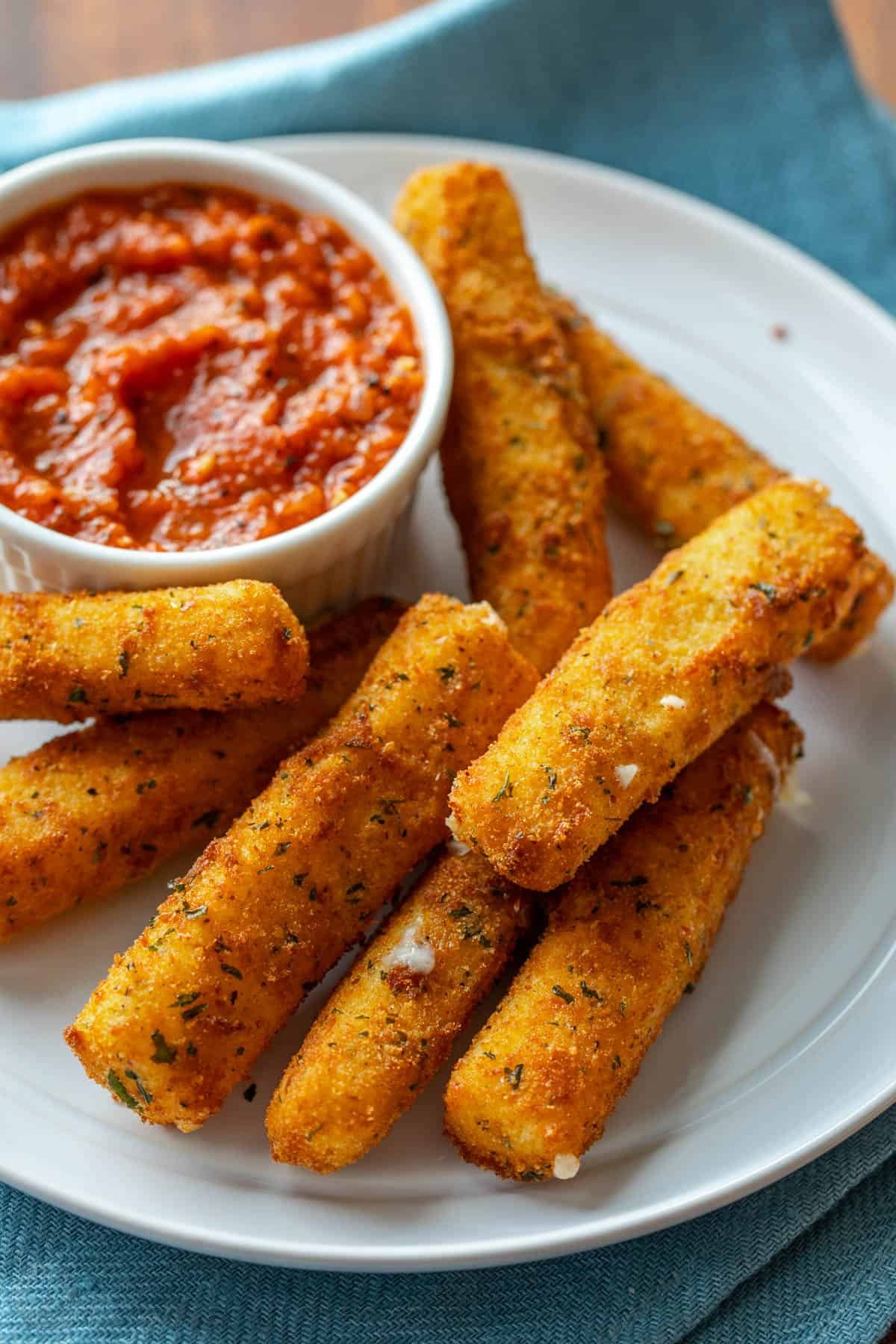 Homemade mozzarella sticks are irresistibly crispy on the outside and gooey and melty in the middle. The ultimate snack or party appetizer! A pile of mozzarella cheese sticks on a white plate next to a bowl of marinara sauce.