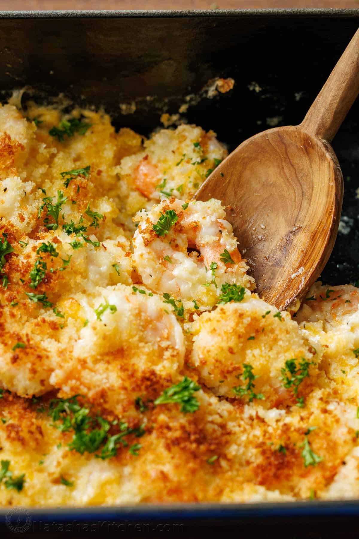 My Shrimp casserole recipe is an easy 30-minute dish for holidays or weeknights alike! Cheesy shrimp filling topped with crunchy breadcrumbs. Shrimp Casserole with breadcrumb topping served out of a dish with a wooden spoon