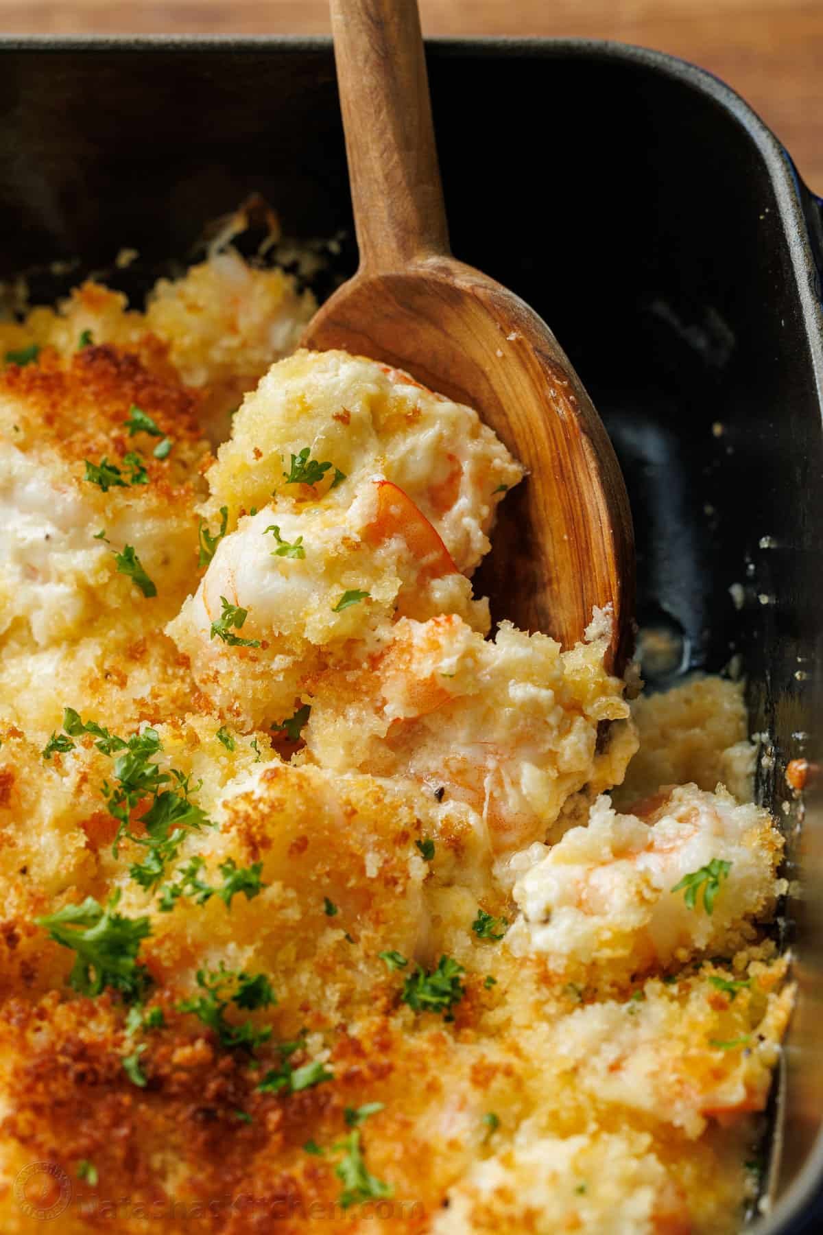 My Shrimp casserole recipe is an easy 30-minute dish for holidays or weeknights alike! Cheesy shrimp bake topped with crunchy breadcrumbs. Wooden spoon scooping shrimp casserole out of a dish