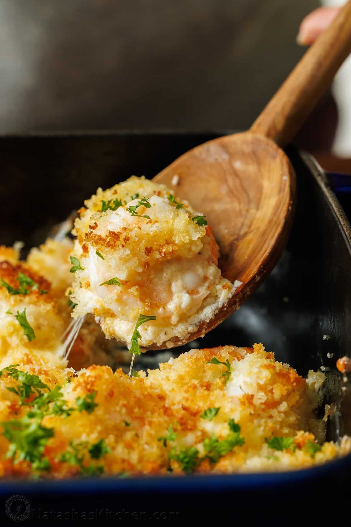 My Shrimp casserole recipe is an easy 30-minute dish for holidays or weeknights alike! Cheesy shrimp filling topped with crunchy breadcrumbs. Seafood bake with breadcrumb topping scooped out of a dark baking dish with wooden spoon