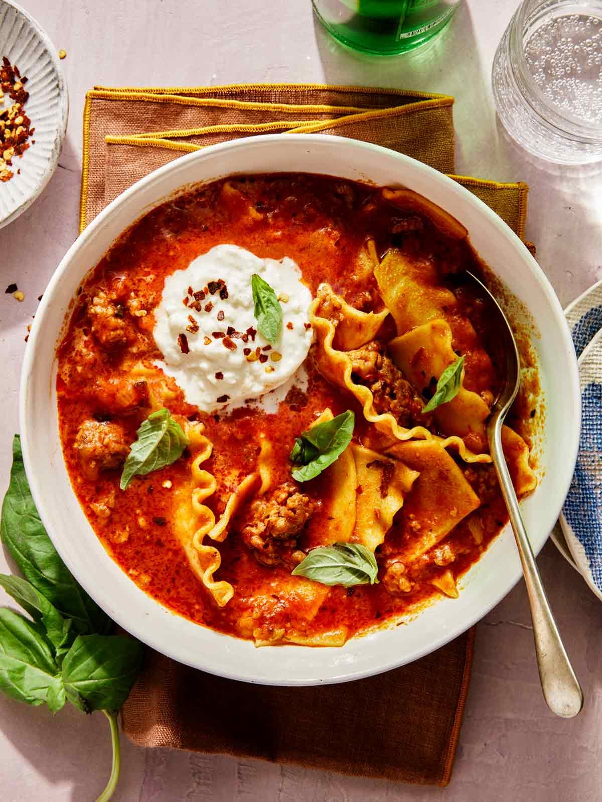Lasagna soup in a bowl with sparkling water on the side.