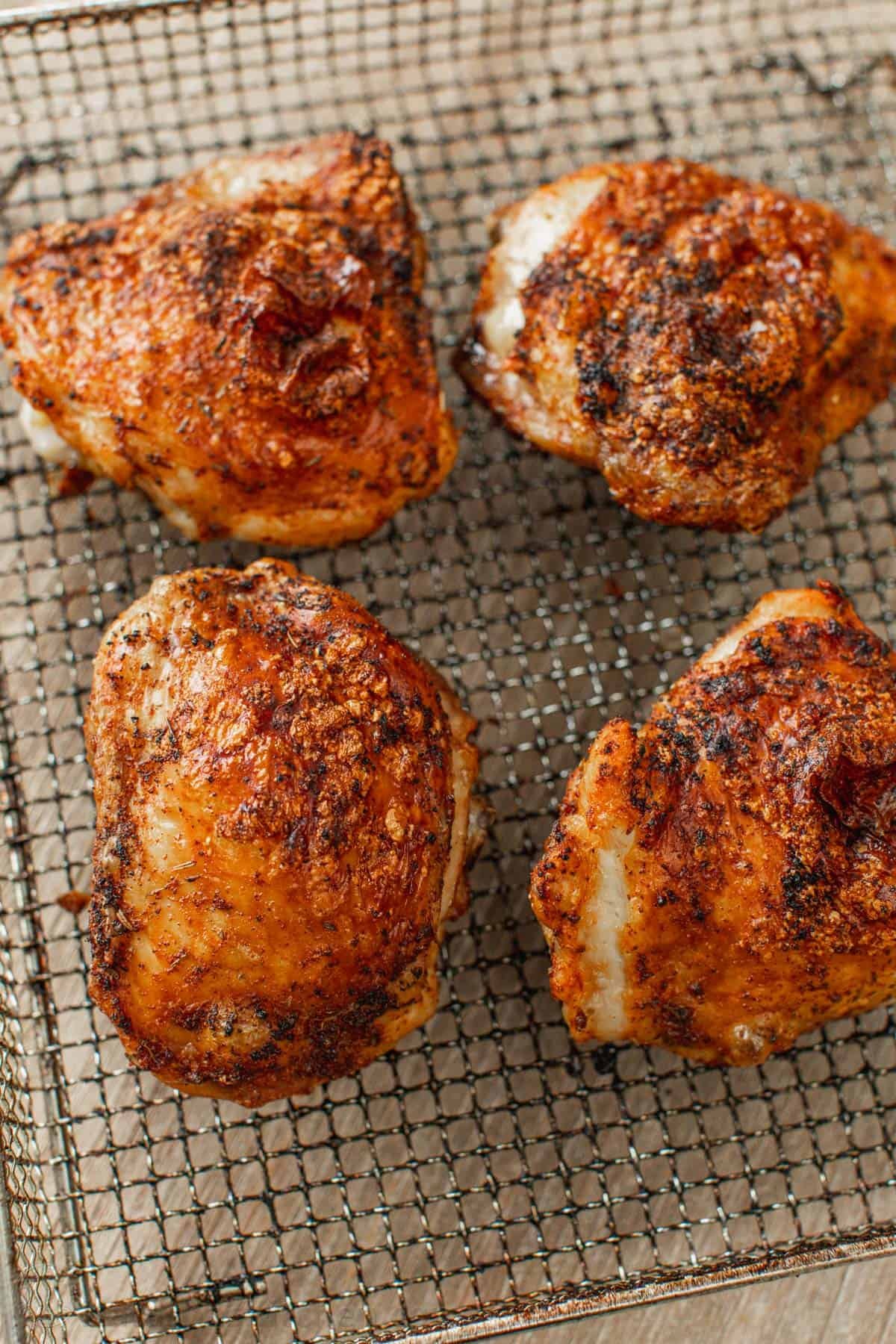 Air fryer chicken thighs are juicy, perfectly seasoned, and ready in a fraction of the time it takes to bake chicken thighs in the oven. Four cooked air fryer chicken thighs in the air fryer basket.
