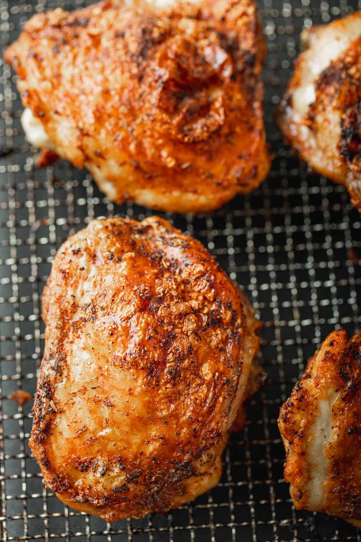 Quick and easy Air Fryer Chicken Thighs with a crisp, salty skin and juicy center. You will love this chicken thigh seasoning! Close up of four cooked air fryer chicken thighs in the air fryer basket.