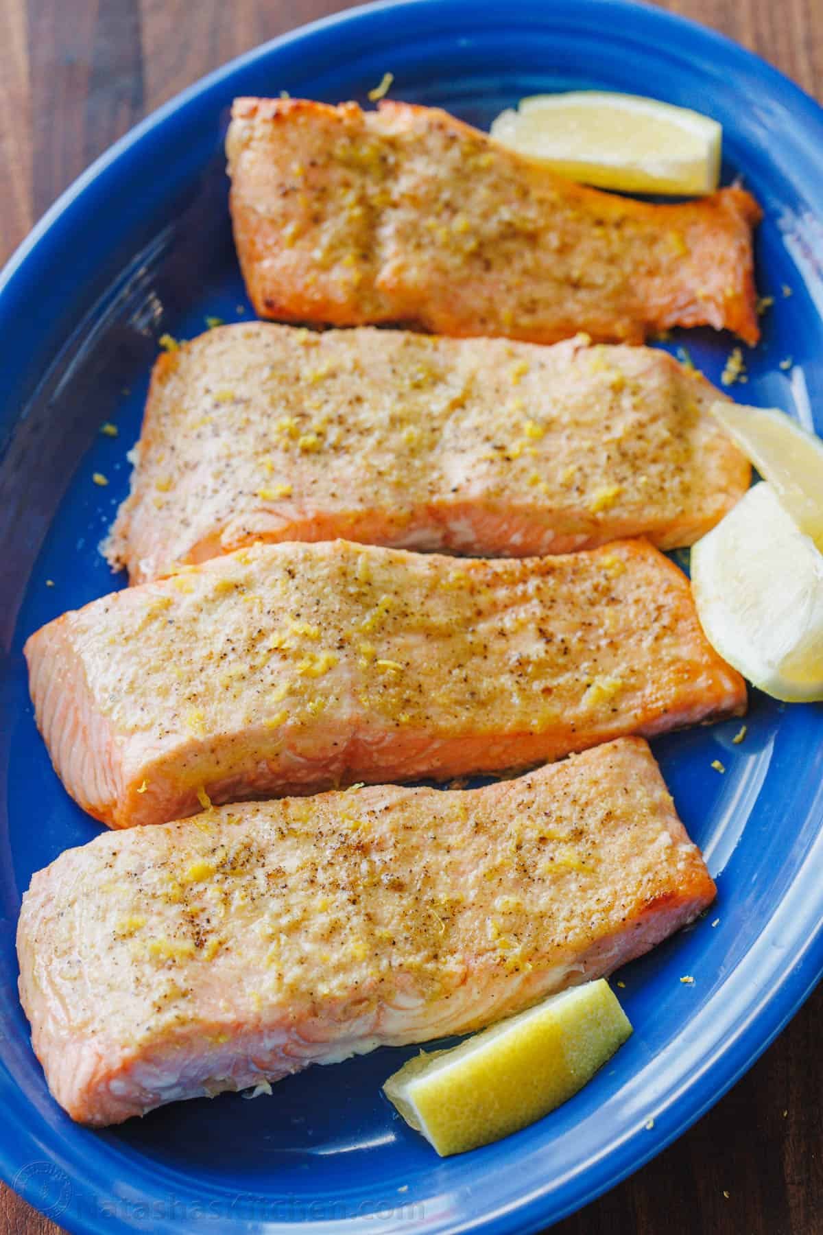 Air Fryer Salmon is one of the best ways to cook salmon in 10 minutes! The air fryer creates a crisp edge with a flaky and juicy center. Four air fryer salmon fillets served on a blue plate with lemon wedges for garnish.