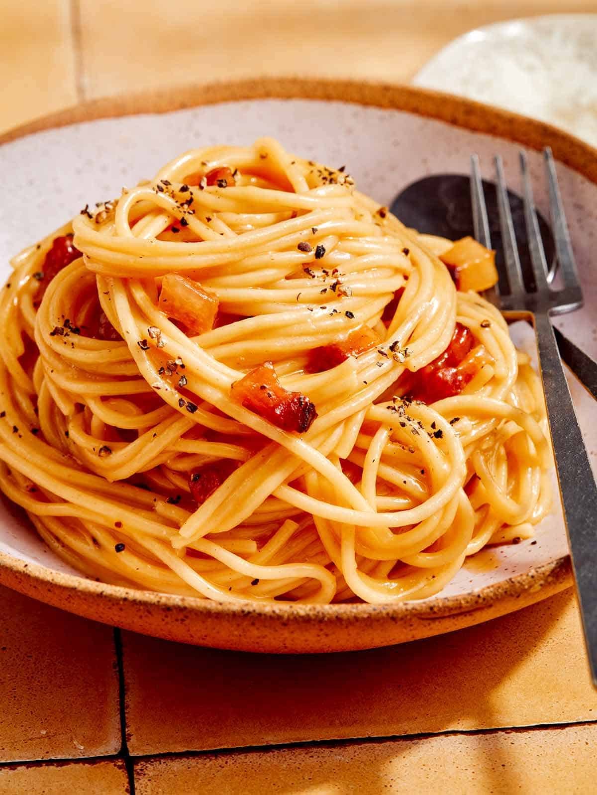 Carbonara in a bowl with a spoon and fork next to it.