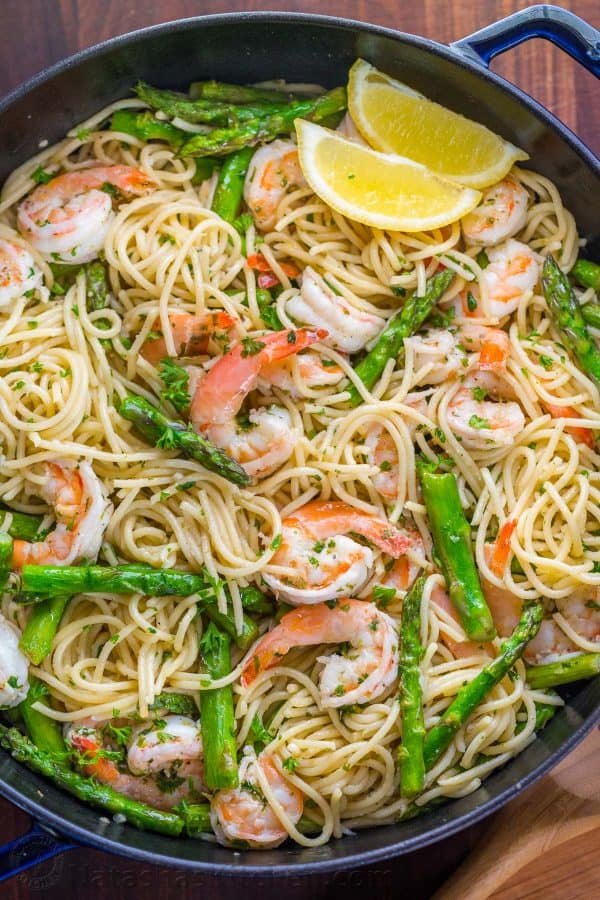 A bowl of pasta with asparagus, shrimp and two wedges of lemon