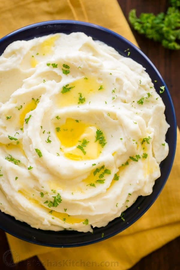 A blue bowl of Creamy Mashed Potatoes garnished with parsley 