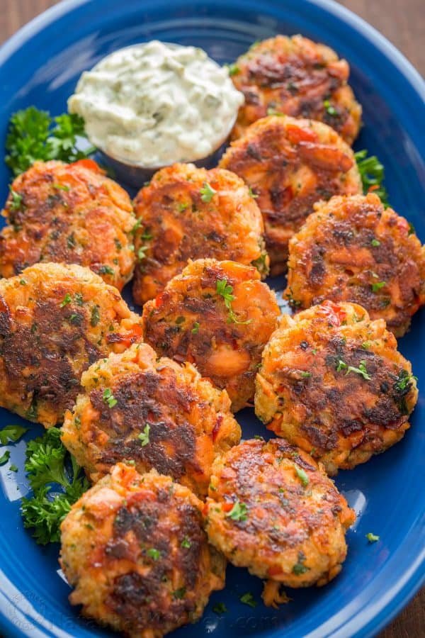 A blue plate with Salmon cakes garnished with parsley and a small bowl of tartar sauce 
