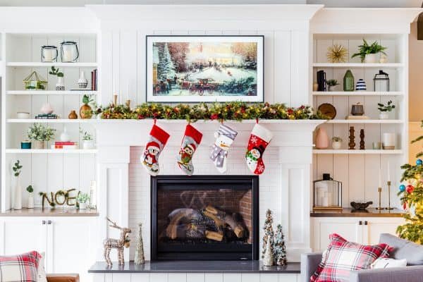 A fire place with four stockings hanging off and Christmas decorations around it 