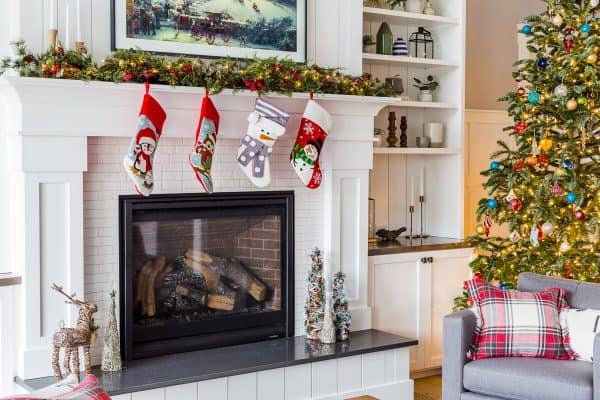 A fire place with four stockings hanging off and Christmas decorations around it 