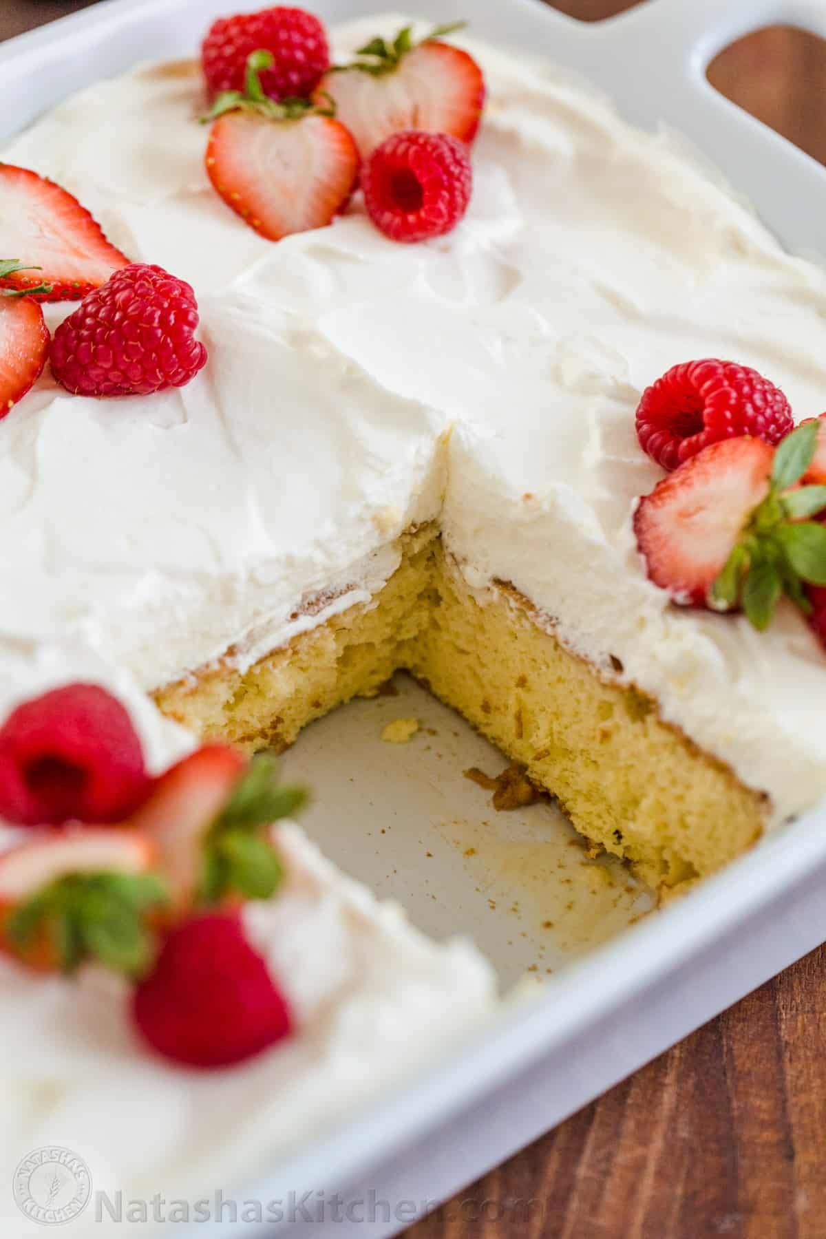 Tres Leches Cake has a soft and ultra-moist crumb. This authentic Tres Leches Cake recipe is soaked with a 3 milk mixture and topped with whipped cream. #tresleches #treslechescake #treslechescakerecipe #mexicancake #cake #cakerecipe #moistcake #natashaskitchen Tres Leches cake in casserole dish with slice removed to show moist layers