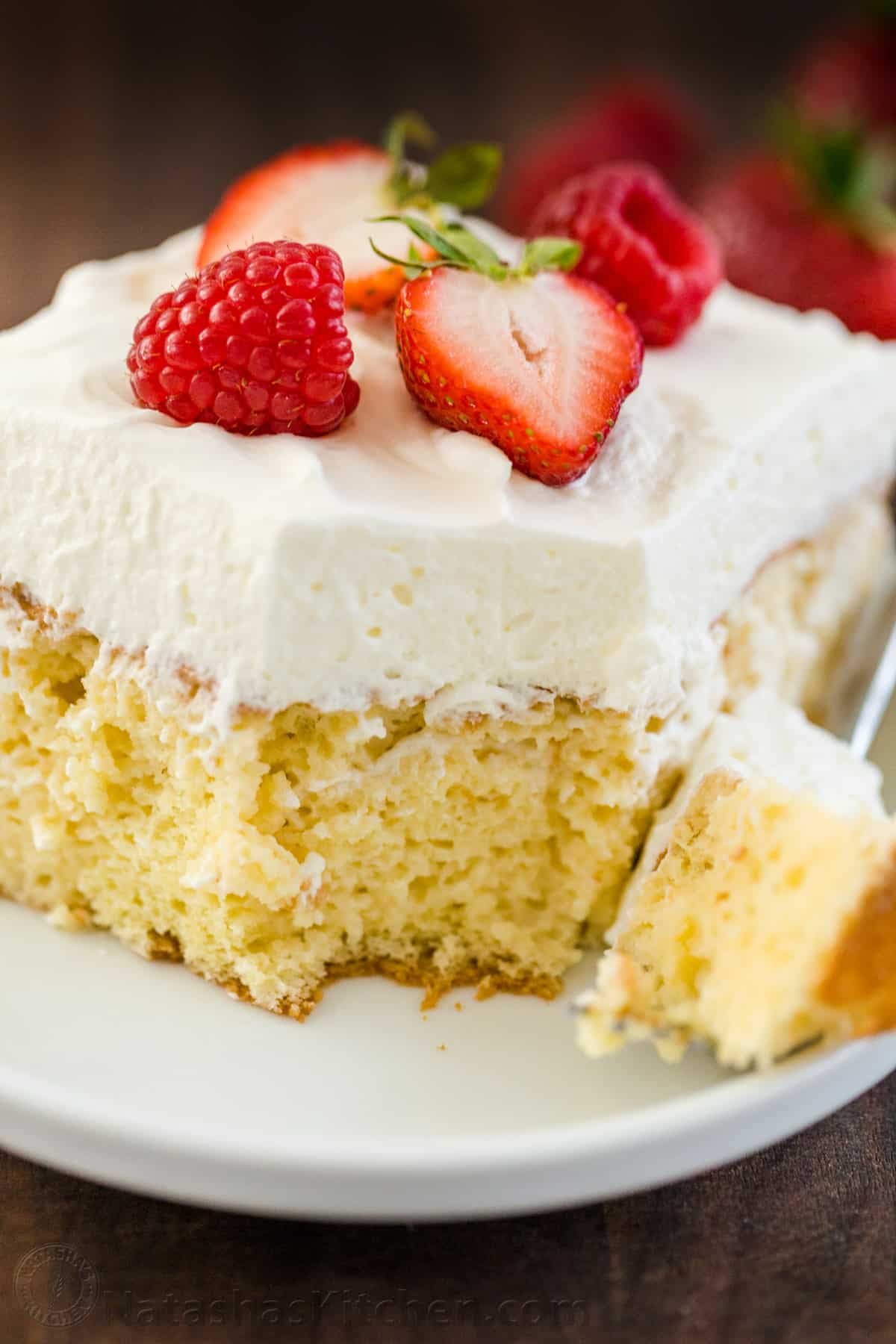 Tres Leches Cake has a soft and ultra-moist crumb. This authentic Tres Leches Cake recipe is soaked with a 3 milk mixture and topped with whipped cream. #tresleches #treslechescake #treslechescakerecipe #mexicancake #cake #cakerecipe #moistcake #natashaskitchen Moist tres leches cake on a plate topped with whipped cream and berries