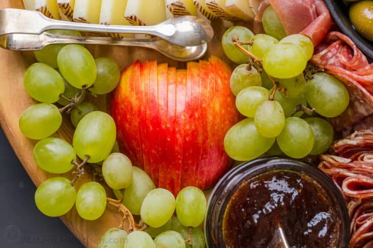 Making a Charcuterie Board is easier than you think. Sharing the best flavor pairings, and tips for arranging a meat and cheese board. Apple sliced for charcuterie with grape segments around it