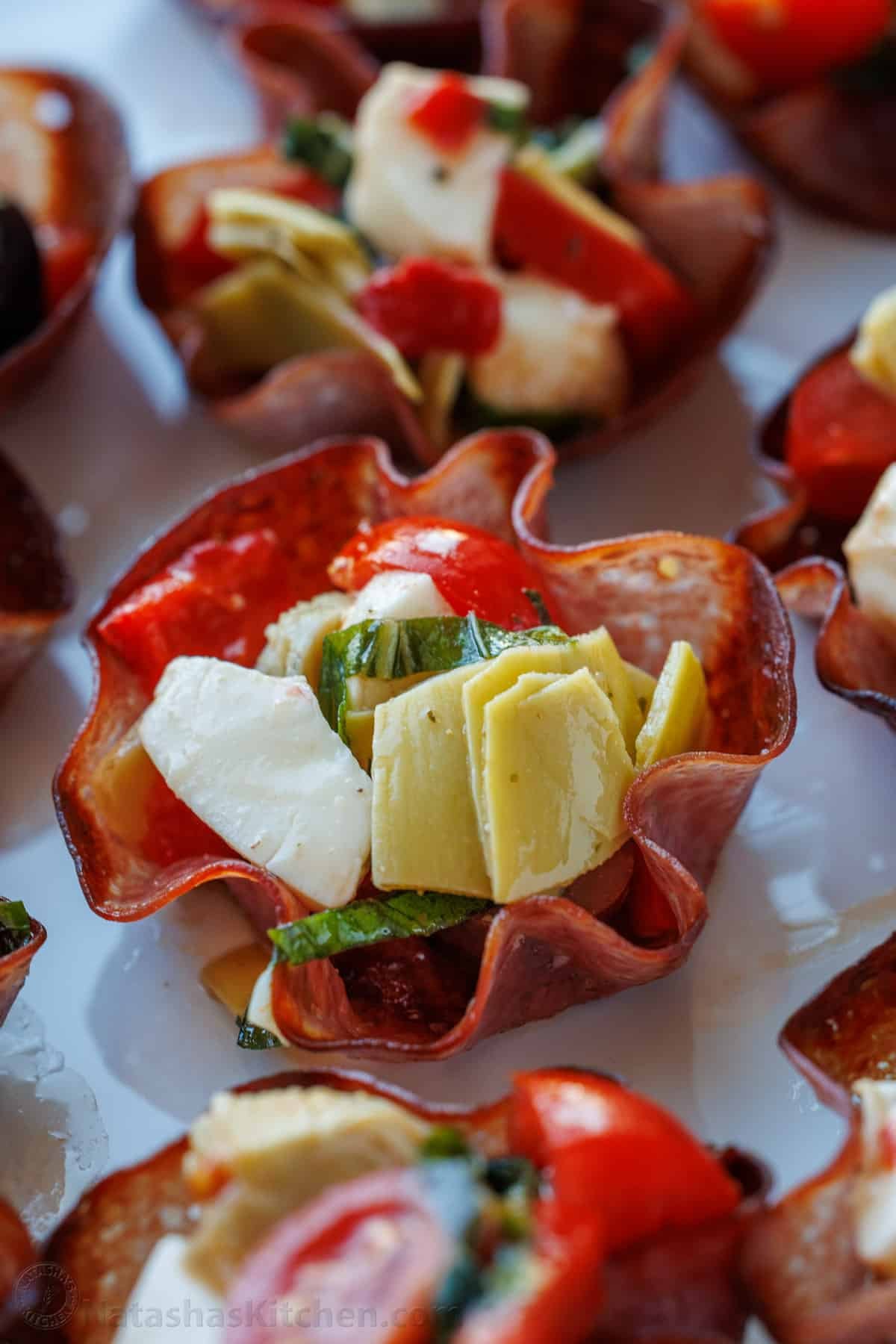 This Salami Cups appetizer recipe is bite-sized perfection! Thin salami baked into crispy cups, filled with your favorite cheeses, antipasto, and herbs. Salami Cups Antipasto, a salami bowl with mozzarella, artichoke hearts, roasted red pepper, mozzarella cheese, and basil inside