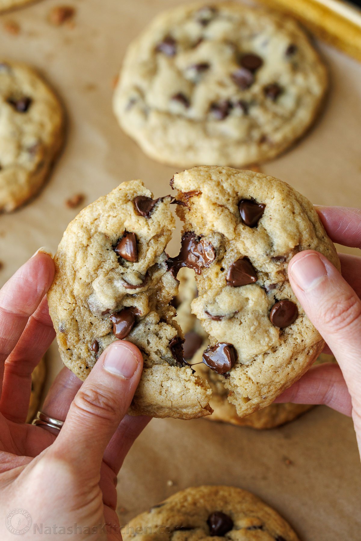 Soft-chewy sourdough chocolate chip cookies made with discard and loaded with chocolate chips. Step-by-step photos and easy video tutorial. two hands pulling apart an easy sourdough chocolate chip cookie using discard