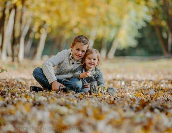 Two children sitting in leaves at the park 
