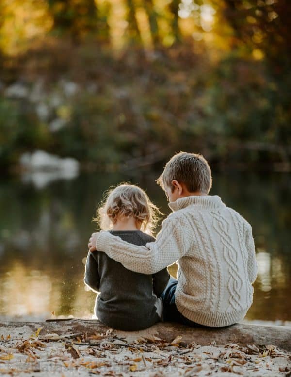 Children sitting on a log next to a river 