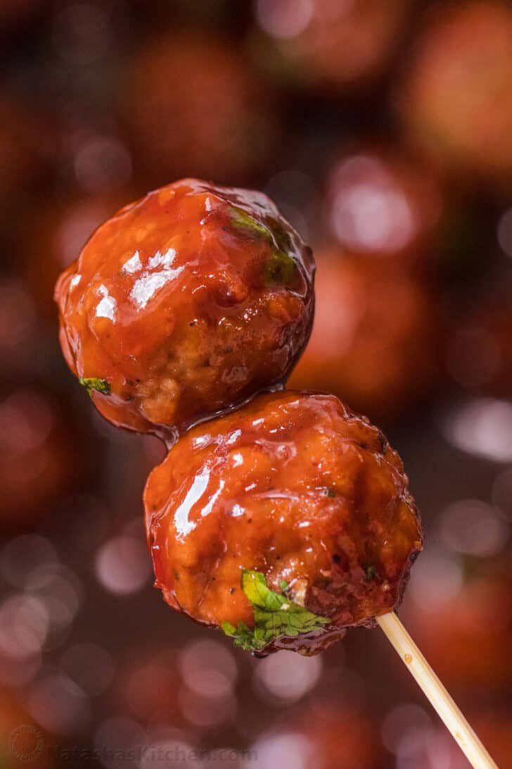 These delicious homemade grape jelly BBQ meatballs are so easy to make and loved by everyone! A toothpick with two meatballs being held.