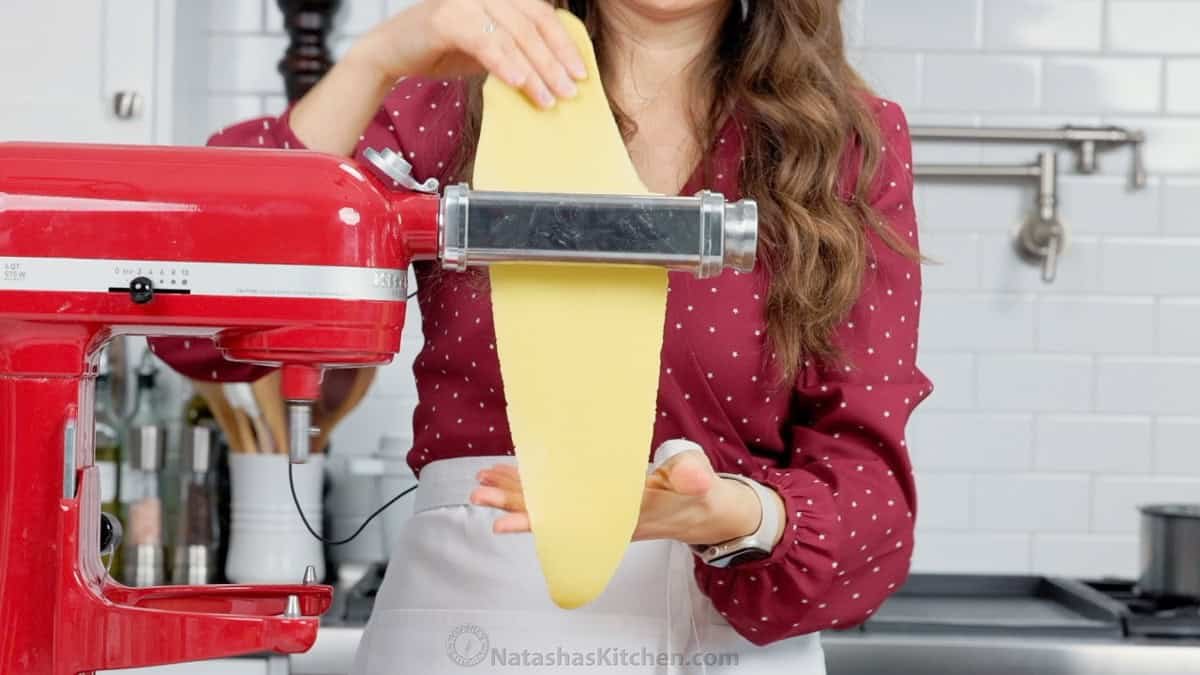 Traditional Angel Wing Cookies (Polish Chrusciki) make a beautiful holiday cookie. These ribbon cookies are dusted with sugar & irresistible. Natasha feeding dough through a pasta roller to make angel wing cookies