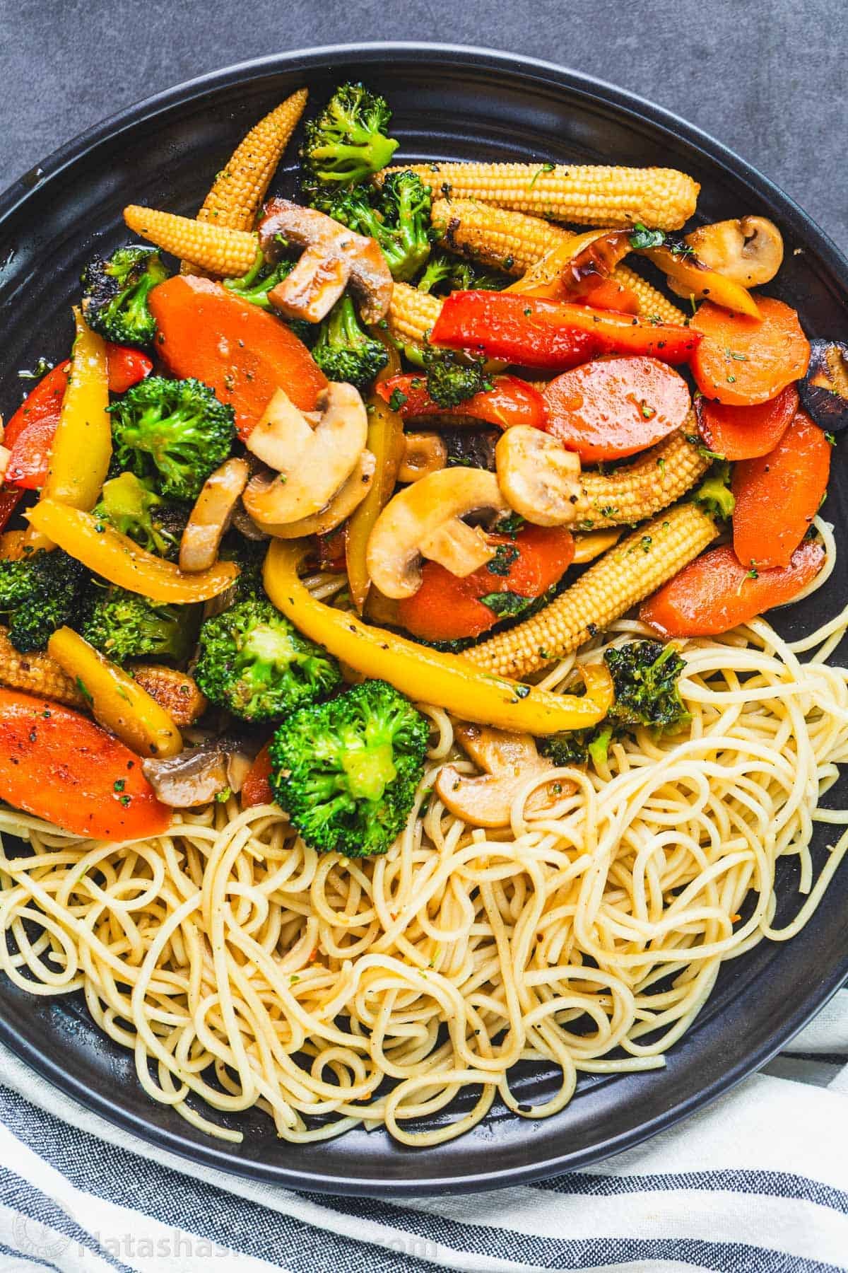 Stir fry vegetables on a plate served with a side of noodles. 