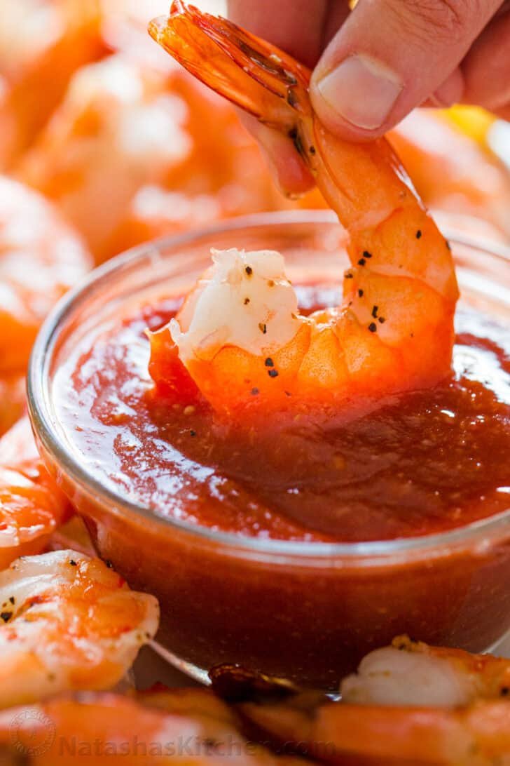Homemade Shrimp Cocktail is impressive and easy with the best oven-baked shrimp and zesty shrimp cocktail sauce. Way better than a store-bought shrimp ring! #shrimpcocktail #shrimpcocktailrecipe #shrimpcocktailsauce #cocktailsauce #homemadecocktailsauce #condiments #dip #shrimp #appetizer #shrimpappetizer Shrimp dipped into shrimp cocktail sauce recipe