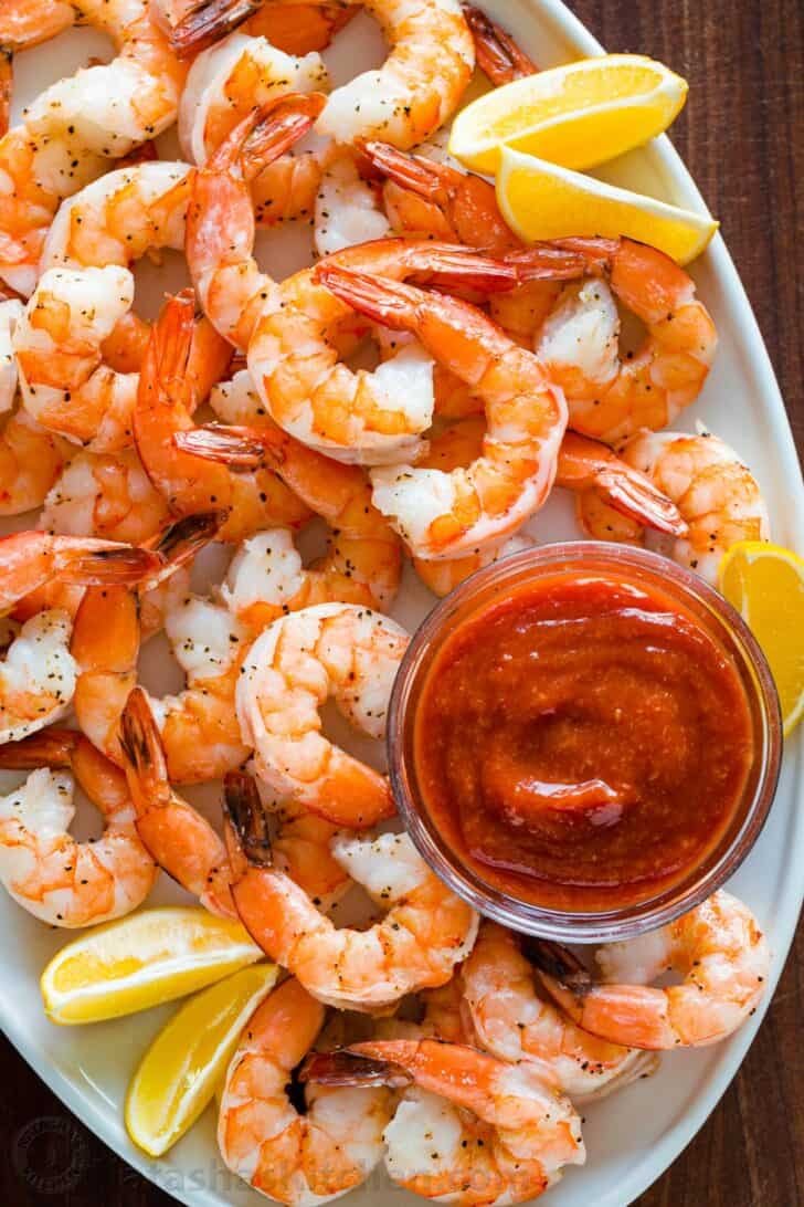 Homemade Shrimp Cocktail is impressive and easy with the best oven-baked shrimp and zesty shrimp cocktail sauce. Way better than a store-bought shrimp ring! #shrimpcocktail #shrimpcocktailrecipe #shrimpcocktailsauce #cocktailsauce #homemadecocktailsauce #condiments #dip #shrimp #appetizer #shrimpappetizer Perfectly baked shrimp on serving platter with shrimp cocktail sauce