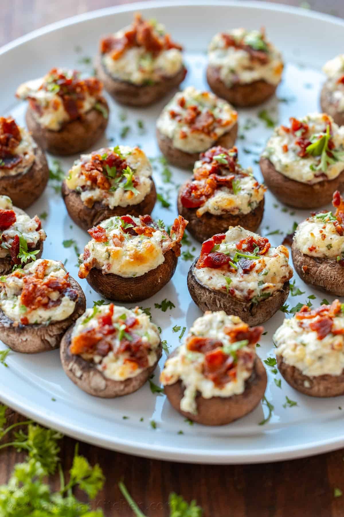 This is the best stuffed mushrooms recipe for your next party. The bite-sized appetizer is stuffed with cream cheese, bacon bites and garlic. White serving platter of baked stuffed mushrooms with cream cheese and bacon