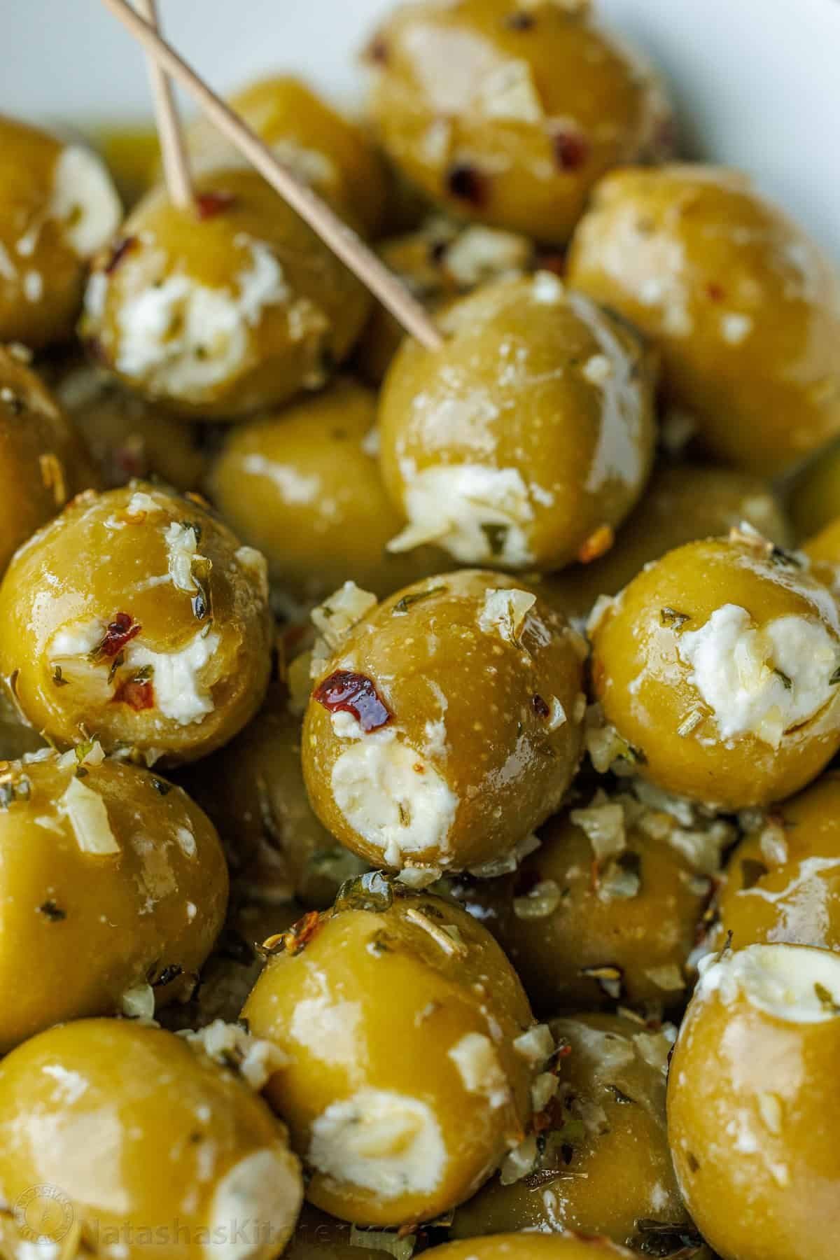 Stuffed Olives are the ultimate no-bake appetizer—quick to make, yet fancy enough for any occasion. They're filled with garlic and herb Boursin cheese and marinated in a flavorful garlic and herb olive oil. A close-up of stuffed olives served on toothpicks.