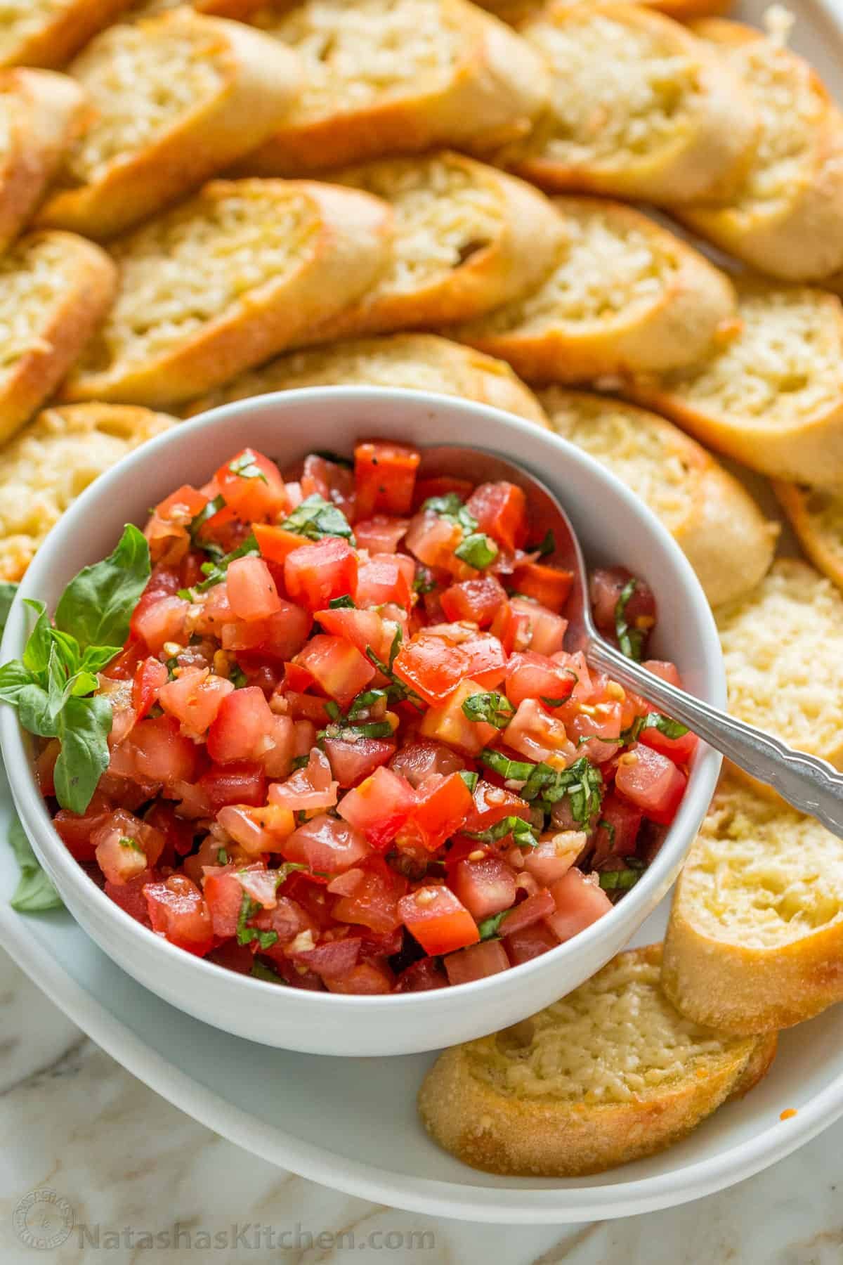 Bruschetta toasts served on a platter with a bowl of tomato topping