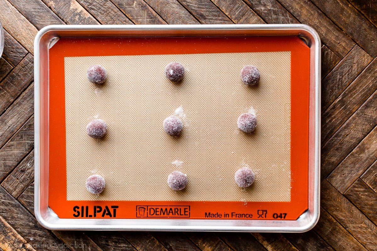 red velvet cookie dough balls rolled in sugar arranged on baking sheet