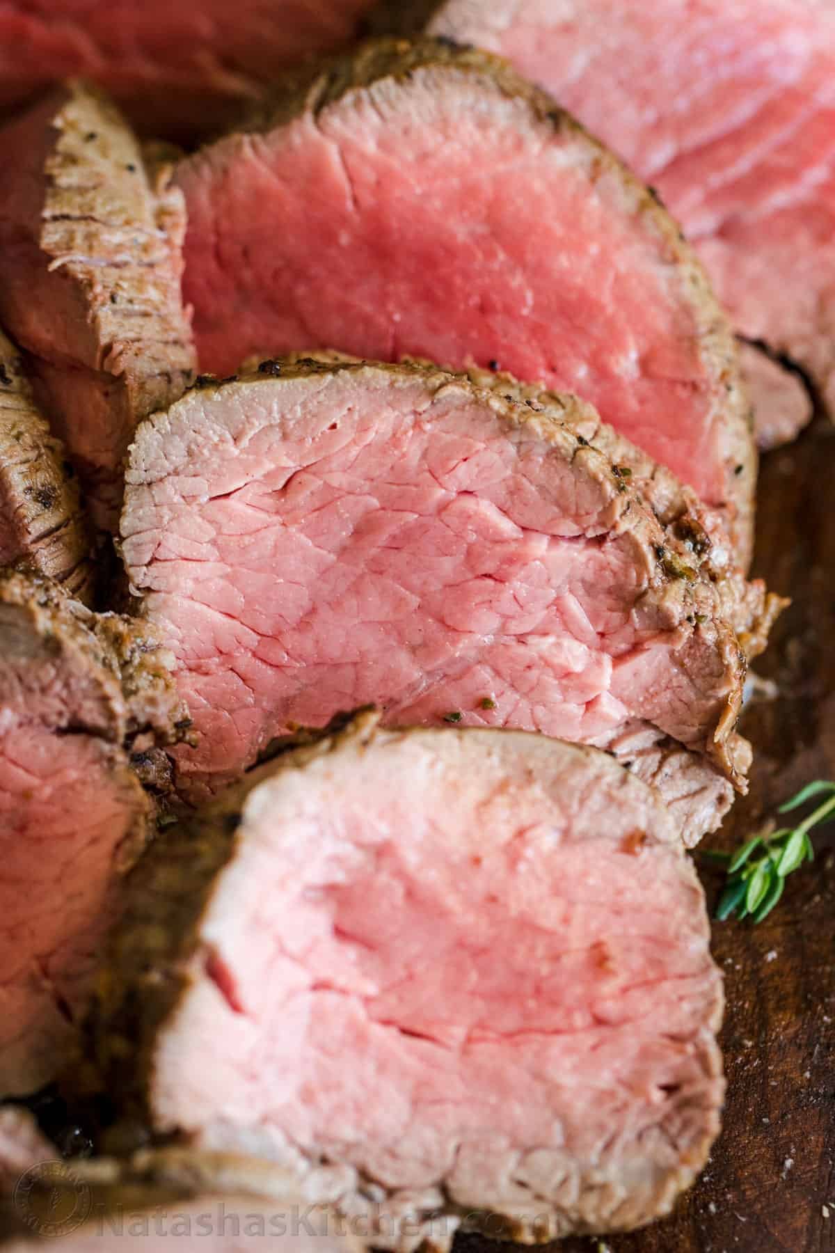 Roasted Beef Tenderloin is a showstopper! This tried and true easy method produces melt-in-your-mouth tender beef. How to trim, tie and cook beef tenderloin. #beeftenderloin #beeftenderloinrecipe #roastedbeeftenderloin #beef #steak #valentinesdaydinner #valentinesdayrecipes #natashaskitchen #dinner #tenderloin Up close slices of roasted beef tenderloin