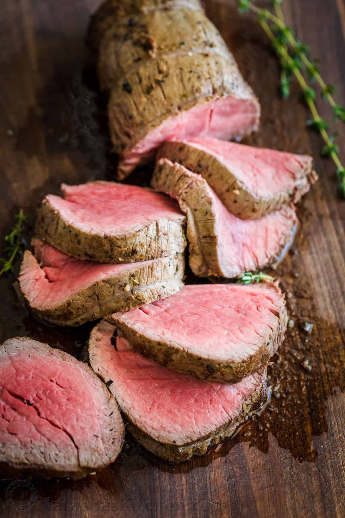 Roasted Beef Tenderloin is a showstopper! This tried and true easy method produces melt-in-your-mouth tender beef. How to trim, tie and cook beef tenderloin. #beeftenderloin #beeftenderloinrecipe #roastedbeeftenderloin #beef #steak #valentinesdaydinner #valentinesdayrecipes #natashaskitchen #dinner #tenderloin Beef tenderloin sliced from a whole filet of beef on cutting board