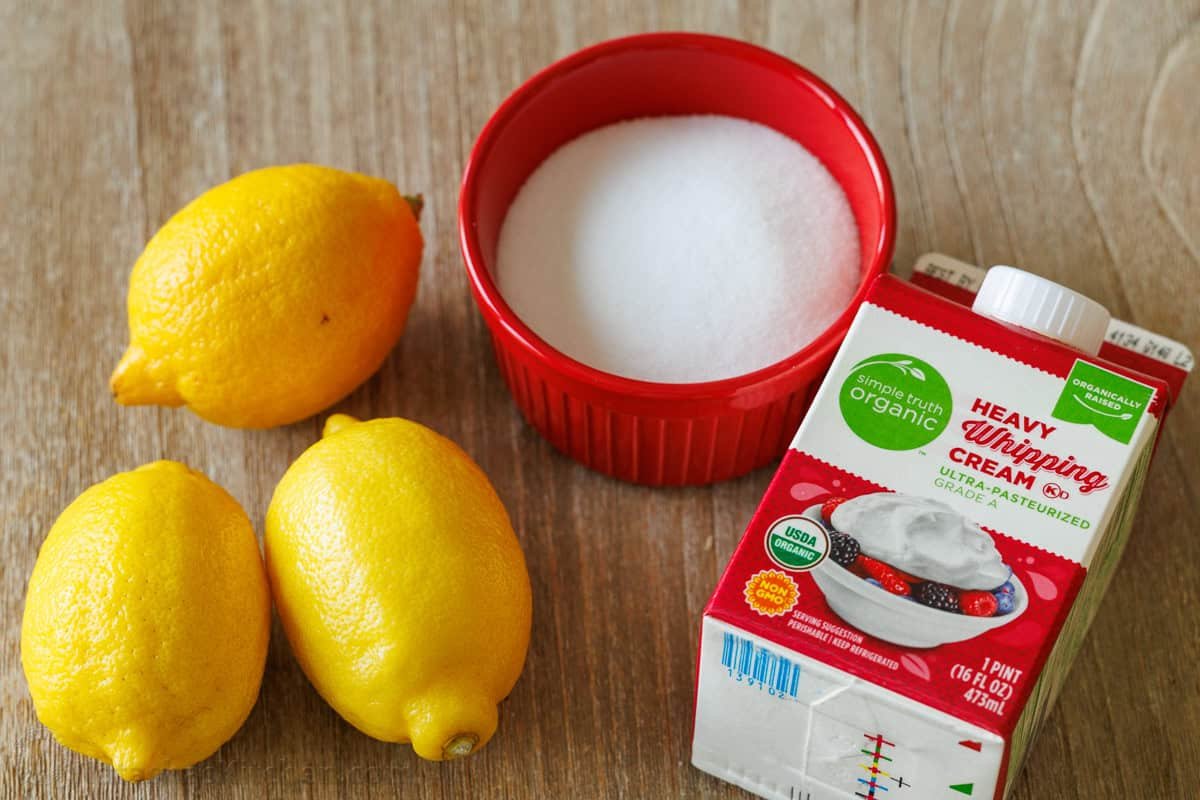 My 3-ingredient Lemon Posset recipe is a velvety smooth lemon custard served in lemon halves. Perfect make-ahead & Cooks in under 10 minutes! ingredients for lemon posset dessert including lemons, sugar and heavy whipping cream