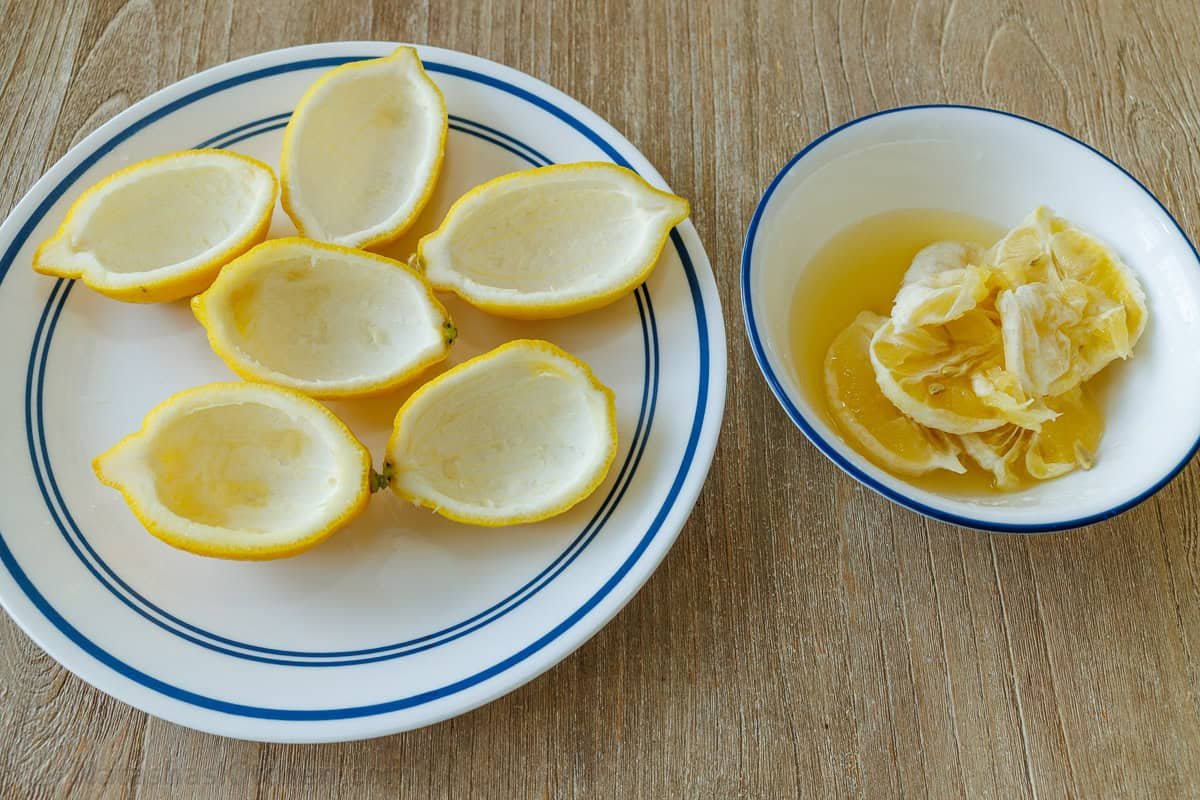 My 3-ingredient Lemon Posset recipe is a velvety smooth lemon custard served in lemon halves. Perfect make-ahead & Cooks in under 10 minutes! Lemon rinds halved and ready for serving with a bowl of lemon juice and membrane in a bowl