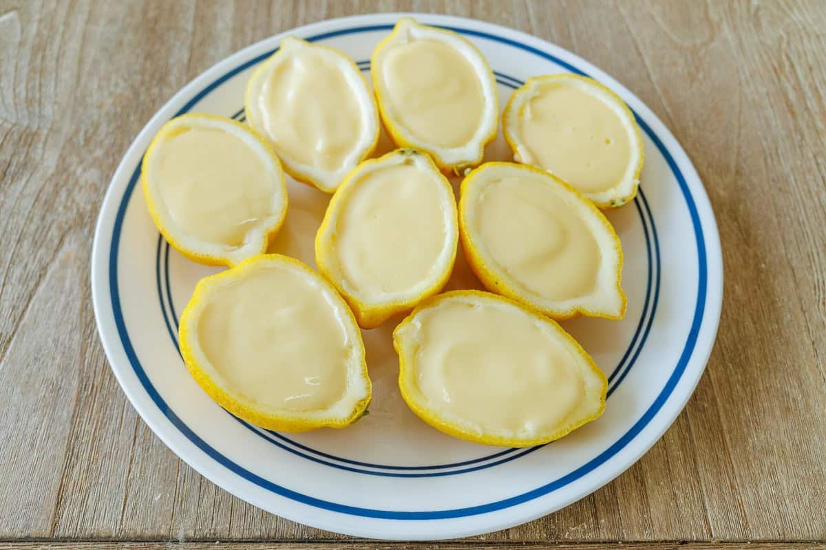 My 3-ingredient Lemon Posset recipe is a velvety smooth lemon custard served in lemon halves. Perfect make-ahead & Cooks in under 10 minutes! Filled citrus cups with custard on a white and blue plate