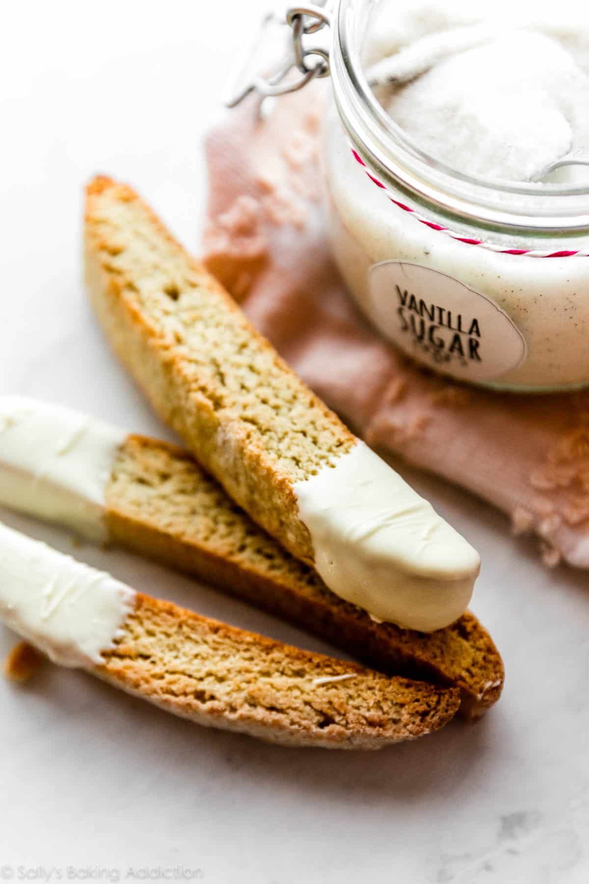 vanilla biscotti cookies dipped in white chocolate and pictured with a jar of vanilla sugar