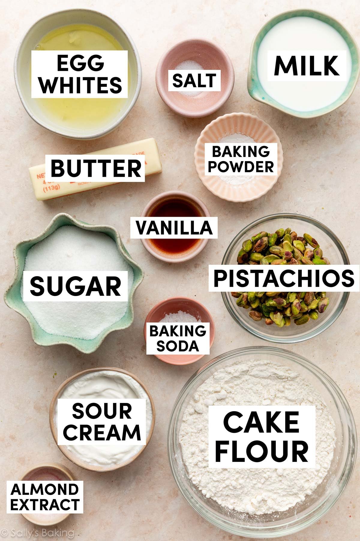 ingredients on peach surface including cake flour, sour cream, milk, egg whites, butter, sugar, almond extract, and vanilla.