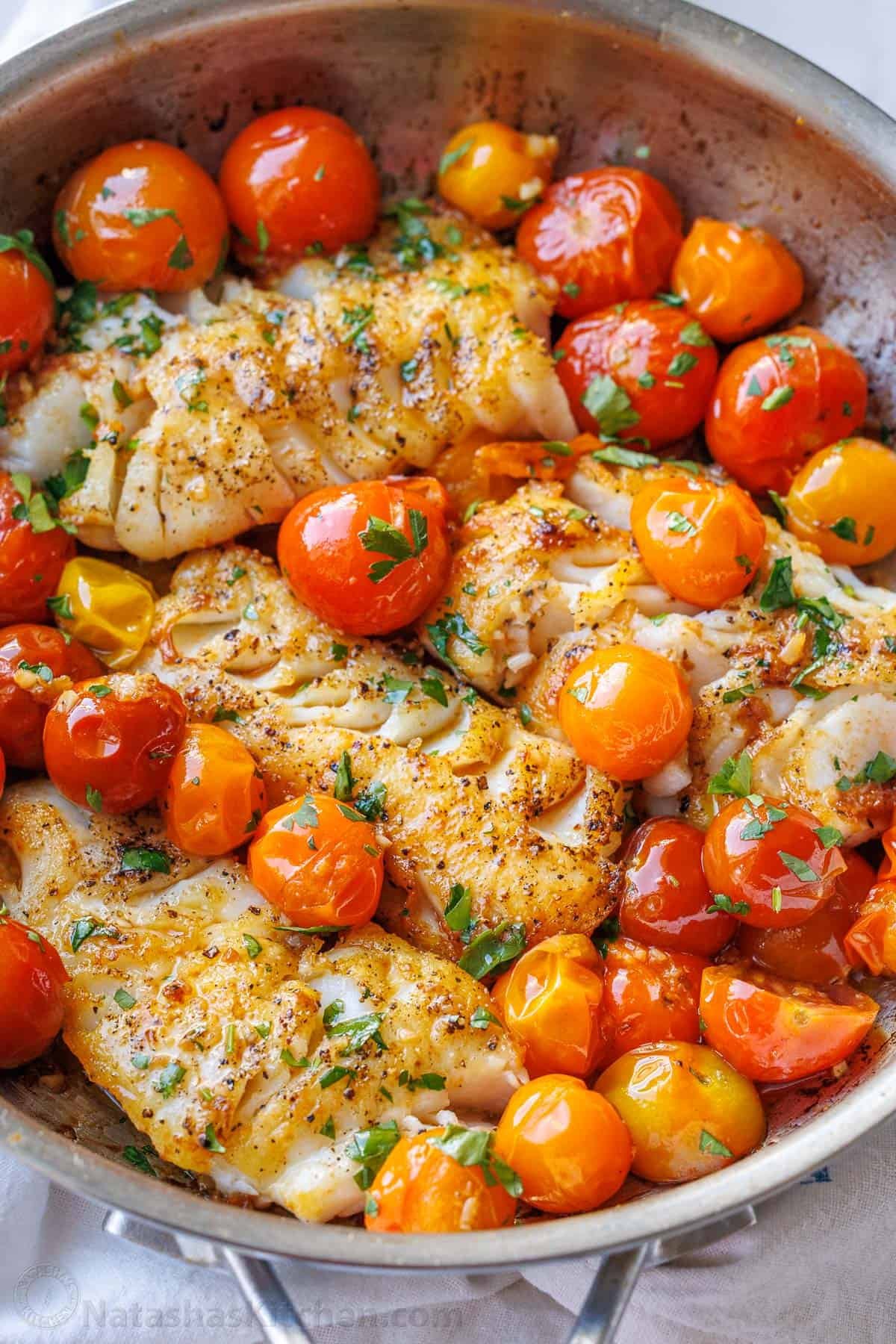 My easy Pan-Seared Cod recipe is flaky and juicy with an incredible tomato, butter, garlic sauce. It cooks in under 15 minutes in 1 skillet! pan seared cod with white wine, tomato, and butter sauce recipe in a skillet with cooked tomatoes and basil garnish