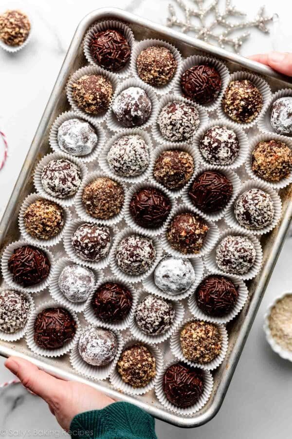 hands holding a tray of rum balls in mini paper liner cups.