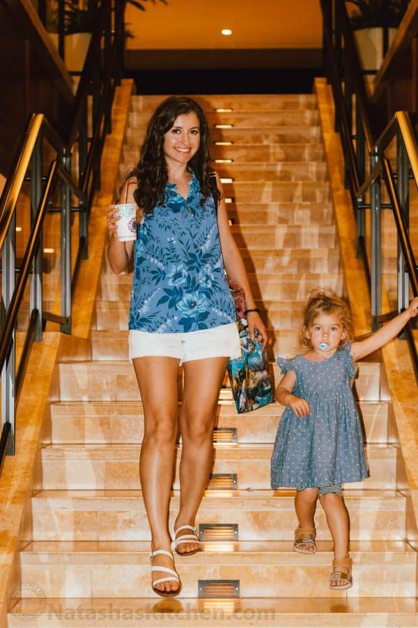 Natasha holding a to-go cup and walking down the stairs with her daughter 
