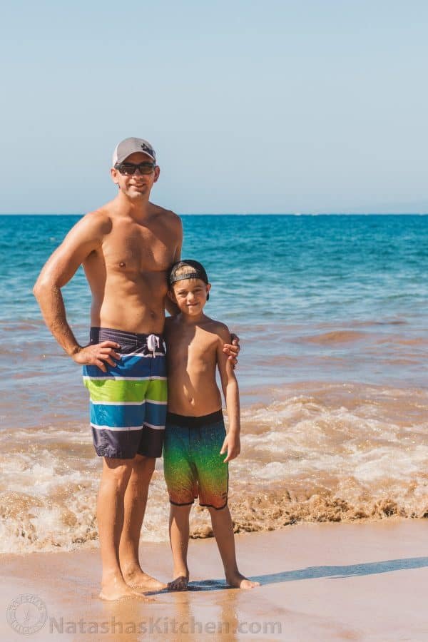 A father and son standing at the beach smiling at the camera
