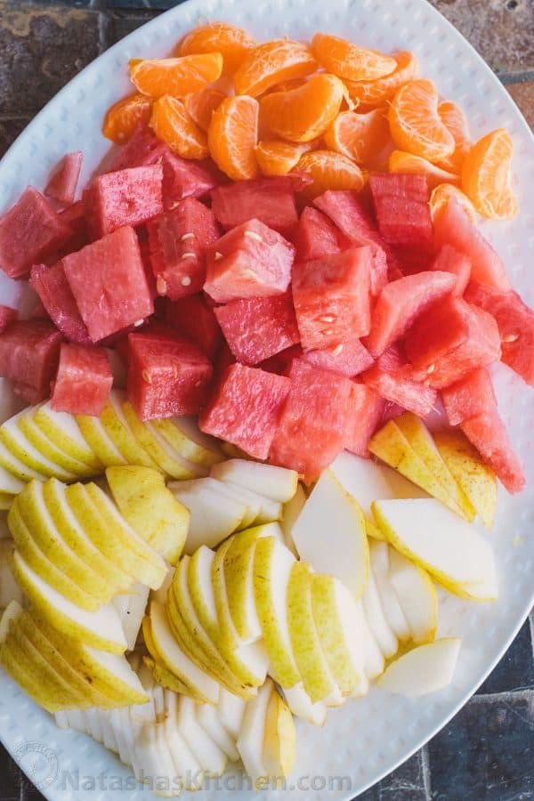 Watermelon, mandarins, and pear cut up and placed onto a plate
