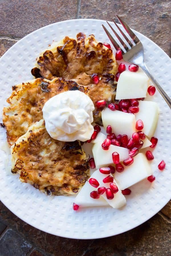 Pancakes on a plate with pears, pomegranate seeds, and whipped cream