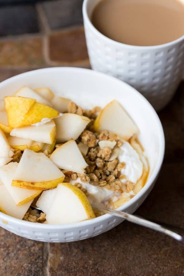 A bowl of food covered in pear slices and a cup of coffee