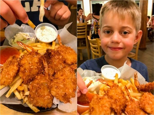 A close up of a basket with fried shrimp, fries and sauces and one of a boy 